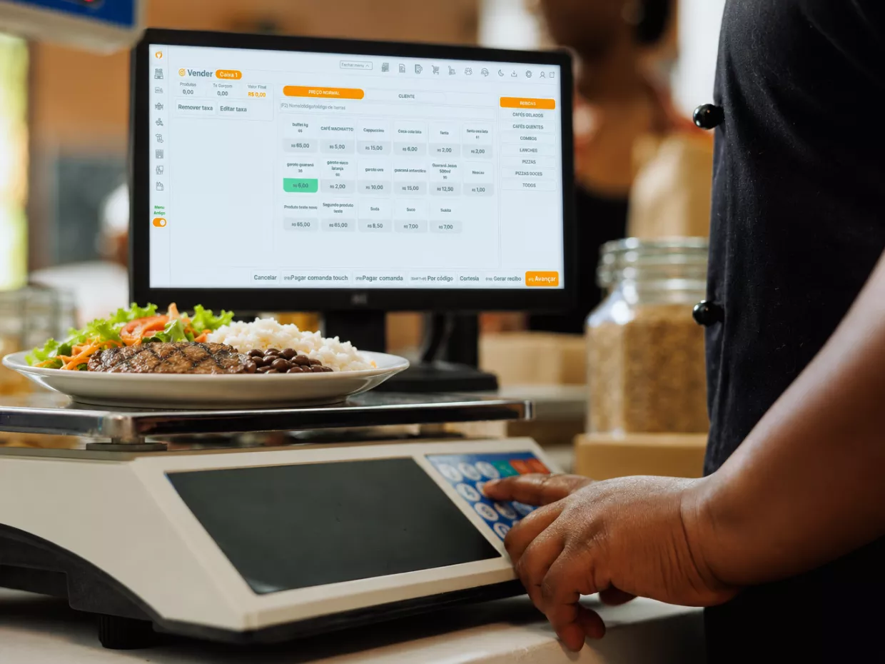Atendente pesando prato na balança integrada ao caixa de um restaurante self-service por quilo